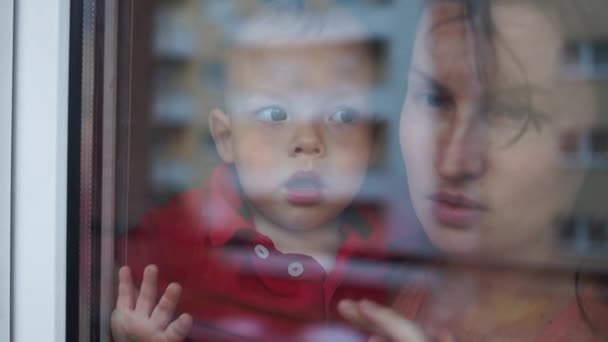 Joven familia, madre y dos niños están de pie en la ventana. Cuarentena y autoaislamiento durante la pandemia del coronavirus Covid-19
 - Metraje, vídeo