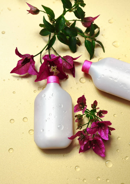 bílá láhev s maskou na vlasy leží na zlatém pozadí s růžovými květy - Fotografie, Obrázek