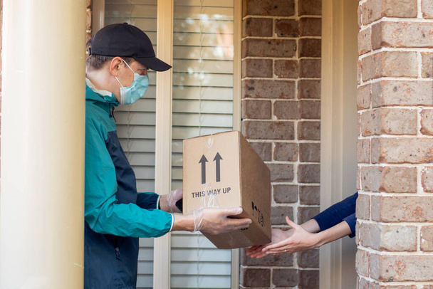 Contactless delivery during COVID-19 pandemic lockdown concept. Courier wearing mask and gloves deliver a parcel to the customer - Photo, Image
