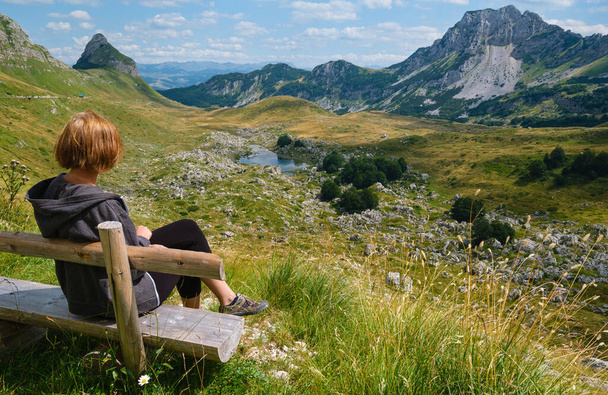 Woman on wooden bench and picturesque summer mountain landscape of Durmitor National Park, Montenegro, Europe, Balkans Dinaric Alps, UNESCO World Heritage.  Durmitor panoramic road, Sedlo pass. - Foto, afbeelding