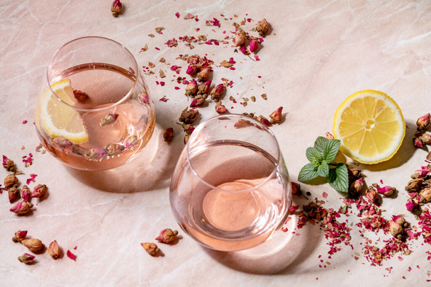 Cocktail glasses of pink rose champagne, cider or lemonade with dry rose buds, lemon and mint. Pink marble background. - Photo, image