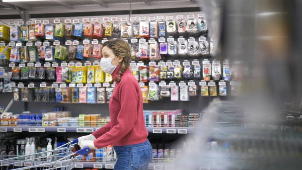 Compras durante la pandemia del coronavirus. Mujer con máscara médica y guantes de goma rueda un carrito de comestibles en un supermercado
. - Foto, imagen