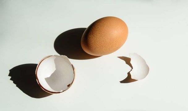 Na bílém pozadí vrhá vejce a vaječná skořápka tmavý stín. . Sluneční osvětlení. Koncept je zdravé stravování, - Fotografie, Obrázek