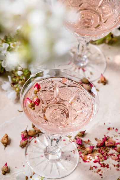 Crystal glasses of pink rose champagne, cider or lemonade with dry rose buds. Blossom cherry branches above. Pink marble background - Fotografie, Obrázek