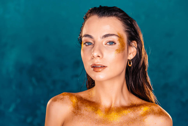 Perfect naked girl covered with gold paint and shimmering sparkles on green wall in studio. Glowing woman, high fashion concept. - Foto, Bild