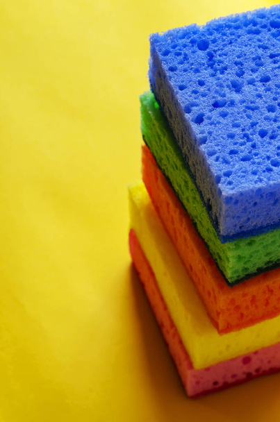 Kitchen porous sponges. A stack of multi-colored kitchen sponges on a yellow background. A set of new bright accessories for cleaning. Commercial cleaning company. Selective focus. - Foto, Imagem