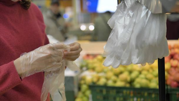 Πανδημία του κορωναϊού. Μια γυναίκα σε ένα σούπερ μάρκετ βάζει πλαστικά γάντια μιας χρήσης για την προστασία από coronavirus, close-up. - Φωτογραφία, εικόνα