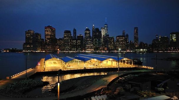 Vista nocturna del horizonte del Bajo Manhattan desde Brooklyn Heights a través de East River, campos de atletismo públicos en el lado de Brooklyn en primera línea, Nueva York, NY, EE.UU. - 5 de abril de 2017
 - Foto, imagen