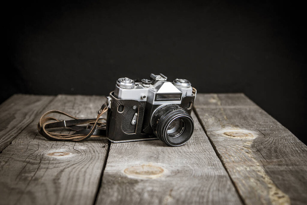 Alte Vintage-Fotokamera mit schwarzem Hintergrund auf einem Holztisch - Foto, Bild
