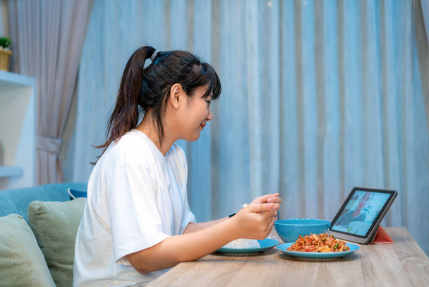 Asyalı bir kadın, sanal mutlu saat yemeği yiyor ve erkek arkadaşıyla internetteki video konferansında dijital tabletle sosyal uzaklık için bir video görüşmesi yapıyor. - Fotoğraf, Görsel