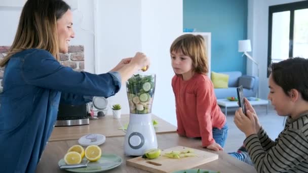 Video of boy helping his mother to prepare a detox juice with blender while his brother take photographs . - Filmmaterial, Video