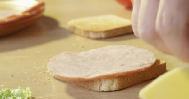 Broodje ham en kaas maken met sla en geroosterd brood op een houten tafel op de keukentafel beschoten met rode camera - Video