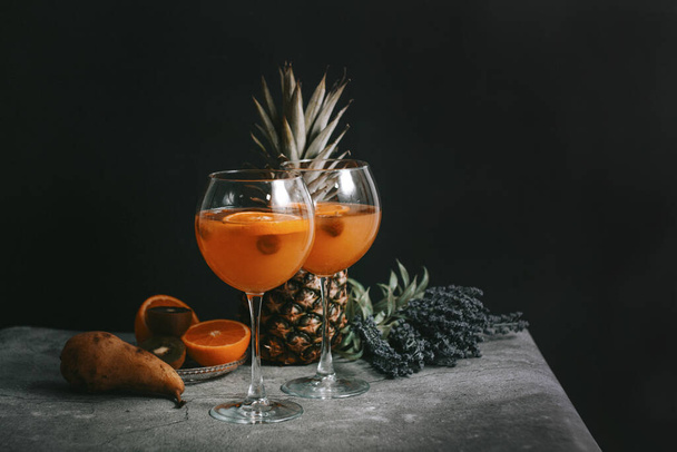 Pomarańczowy koktajl wódki w eleganckim kieliszku do wina z kiwi, ananasem i malinami - Zdjęcie, obraz