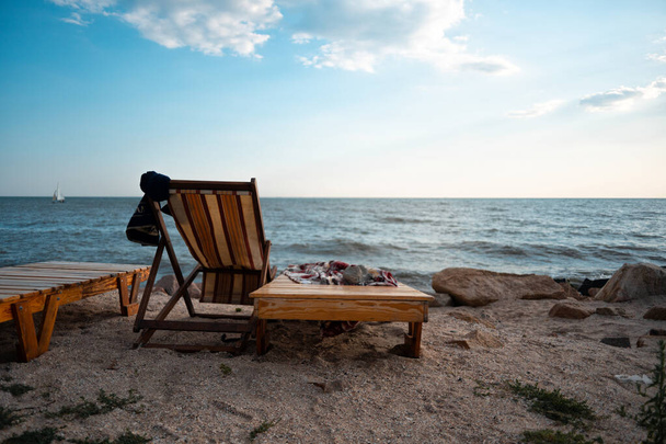 Liegestuhl aus Holz am Meer. Asowsches Meer. Der Stein wird auf ein Handtuch gelegt, damit er nicht wegfliegt - Foto, Bild
