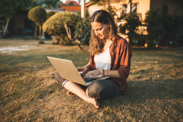 Young woman with laptop sitting on green grass - Foto, Imagen