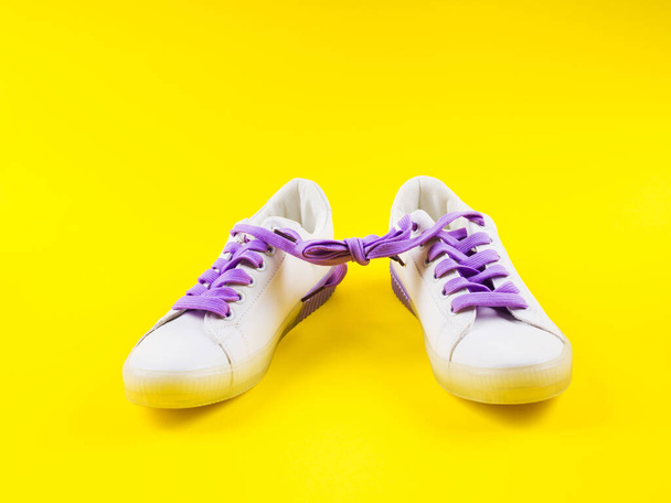Zapatillas blancas con cordones morados sobre fondo amarillo
 - Foto, imagen