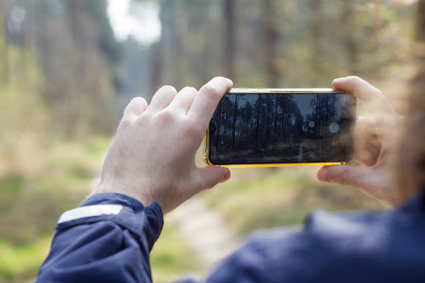 Man making photo on smartphone in forest, smartphone in hands, male photographing on mobile phone outdoor - Фото, изображение