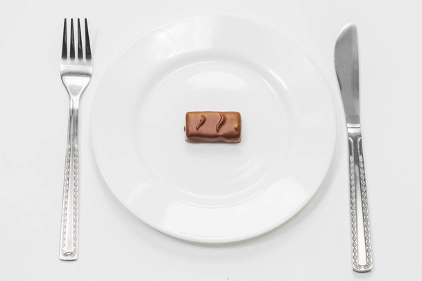 Chocolate bars on white plate with fork and knife on white background. Unhealthy high-calorie diet - Fotoğraf, Görsel
