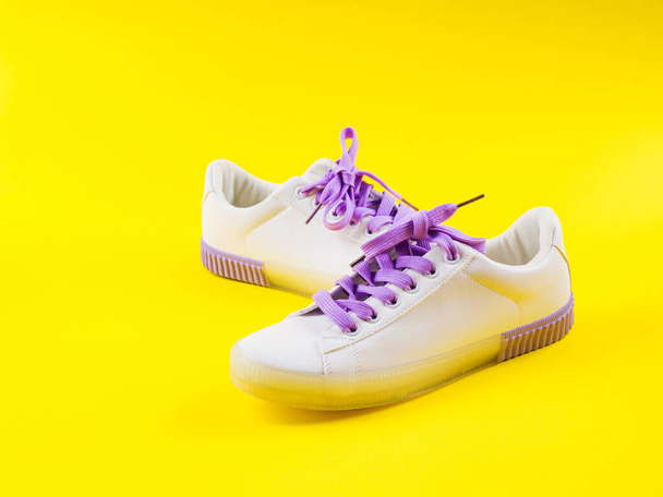 Sneakers bianche con lacci viola su sfondo giallo
 - Foto, immagini