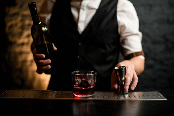 Bartender holding steel jigger which stands on bar counter. - Photo, image