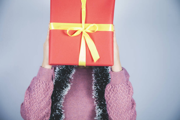 woman hand gift box on face on gray background - Φωτογραφία, εικόνα
