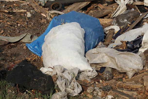 Μια λευκή σακούλα σκουπιδιών κείτεται σε ένα σωρό σκουπίδια στο δρόμο. - Φωτογραφία, εικόνα
