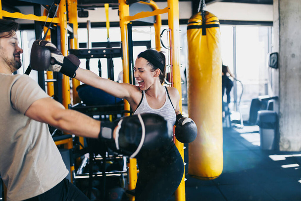 Young attractive woman with instructor on kickboxing training. She hitting or punching in big yellow boxing bag. - Fotoğraf, Görsel