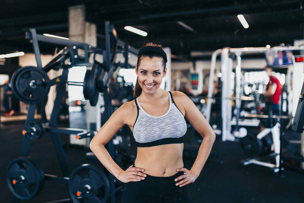 Young attractive woman after successful workout posing and smiling in modern fitness gym - Zdjęcie, obraz