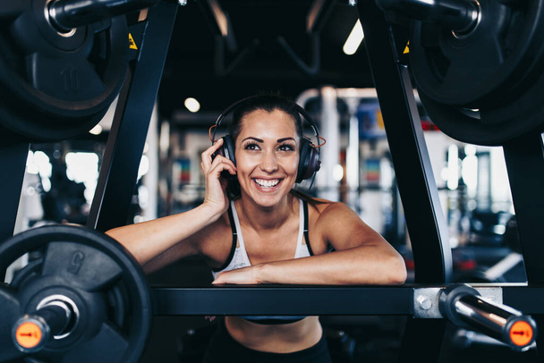 Young attractive woman after successful workout in modern fitness gym dancing, smiling and singing. She listening to music with bluetooth headset and smart phone. - Φωτογραφία, εικόνα