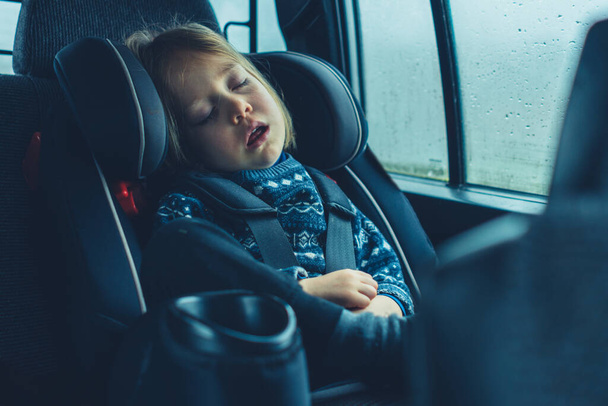A little boy is sleeping in his car seat on a rainy day - Zdjęcie, obraz