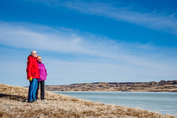 Senior couple standing overlooking an ice-covered Lake Diefenbaker - Photo, Image