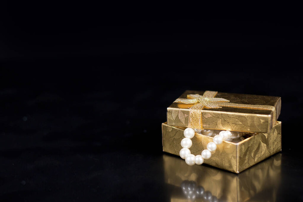Golden jewellery box with shiny pearls on a black glossy background - Photo, Image
