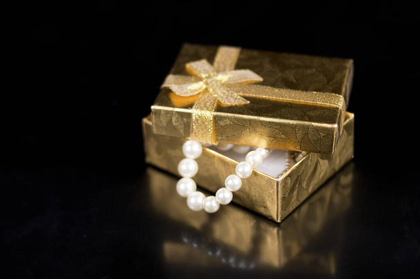 Golden jewellery box with shiny pearls on a black glossy background - Photo, Image