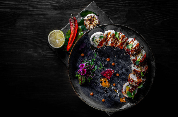 sushi roll with cream cheese, cucumber and eel in plate on black wooden table background - Foto, Imagem