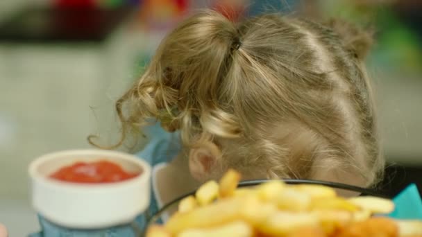 kis aranyos szőke lány eszik sült krumplit az ujjaival, és mártogatja őket ketchup közelről. - Felvétel, videó