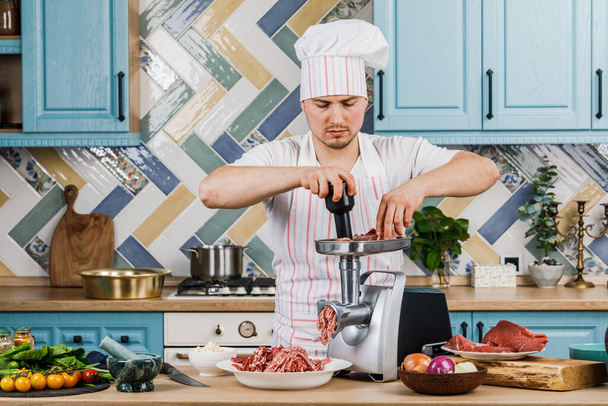 Carne crua. O processo de preparação de carne picada é realizado usando um moedor de carne. Um chef masculino usa um moedor de carne na cozinha - Foto, Imagem