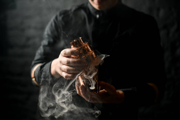 Close-up of bartenders hands which holds smoky steel shaker. - Foto, afbeelding