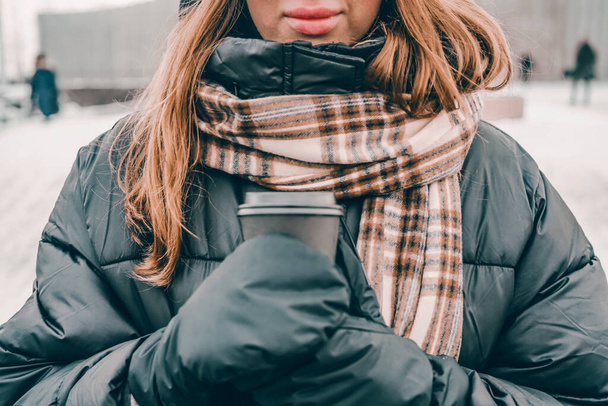 A nő fekete kabátban és meleg sálban tartja a kávét. Reykjavik, Izland 2020. január - Fotó, kép