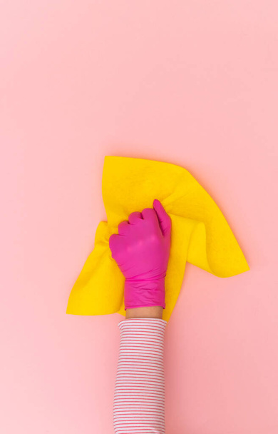 Ręka kobiety w różowej rękawicy ochronnej z żółtą wycieraczką na różowym tle. Widok z góry, przestrzeń kopiowania. - Zdjęcie, obraz