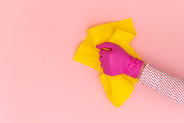 Ręka kobiety w różowej rękawicy ochronnej z żółtą wycieraczką na różowym tle. Widok z góry, przestrzeń kopiowania. - Zdjęcie, obraz