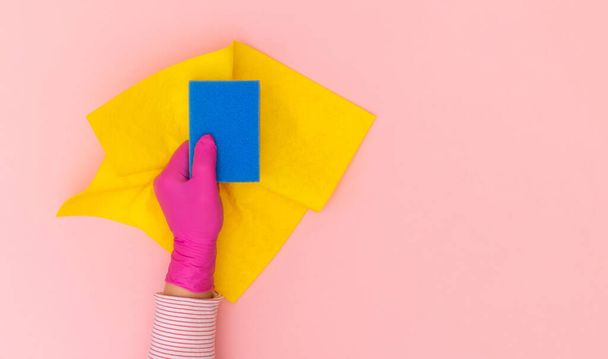 Female hand in pink protective glove with yellow and blue wiper on the pink background. Top view, copy space. - Foto, immagini