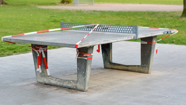 Τραπέζι πινγκ-πονγκ κλειστό με ταινία φραγμού σε ένα πάρκο λόγω του ιού Corona από το πλάι - Φωτογραφία, εικόνα
