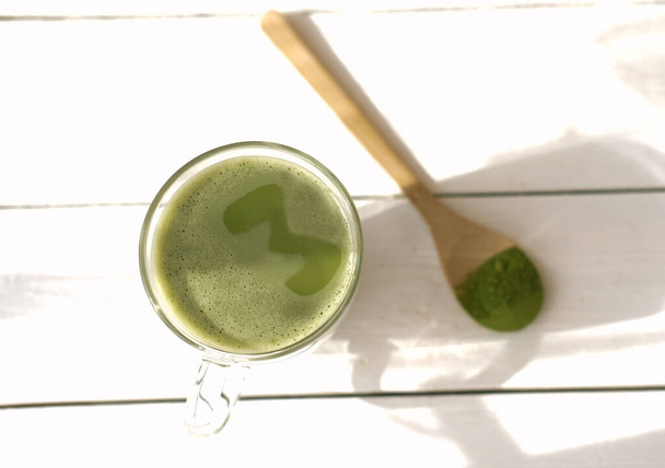 matcha latte in a mug and matcha powder in wooden spoon. healthy drinks concept. modern fashionable drink for weight loss and energy boost. top view - Photo, Image