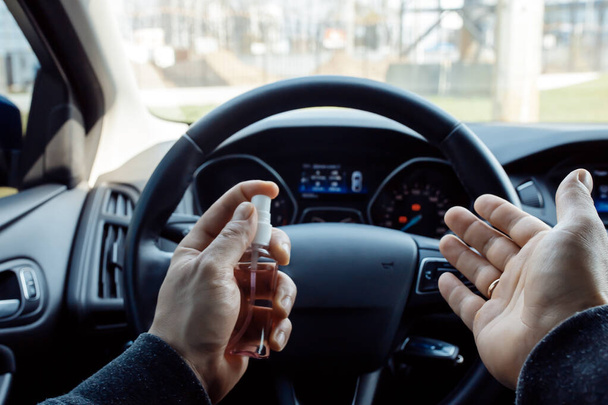 muž rukou rozprašuje dezinfekci alkoholu na volant v autě, proti novelu koronaviru nebo Corona Virus Disease (Covid-19). Antiseptický, hygienický a zdravotní koncept - Fotografie, Obrázek