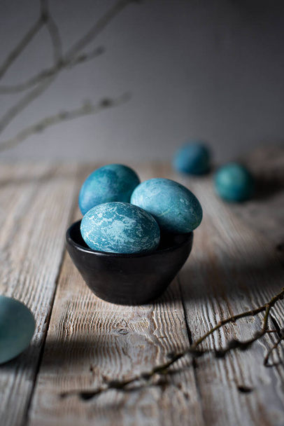 colored marble eggs lie in a cup, next to a willow branch, as a symbol of Easter, on a wooden table. rustic  - Foto, imagen