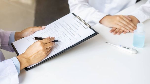 Doctor consulting patient, working on diagnostic examination on Coronavirus disease while writing on prescription record information document in clinic or hospital office. Medical and Health concept. - Photo, Image
