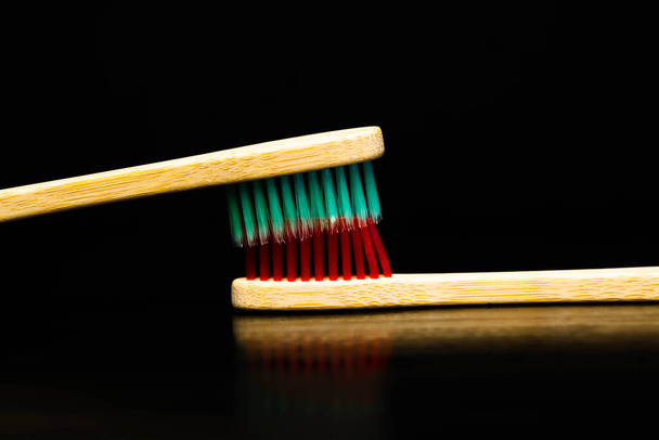 Dental and oral care products. Hygiene of teeth and oral cavity. Wooden toothbrush red and green. Black background - Photo, Image
