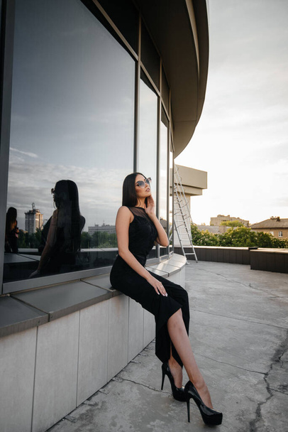 Stylish young and sexy girl posing in front of a business center in black. Fashion and style - Фото, изображение