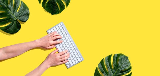 Personne utilisant un clavier d'ordinateur avec des feuilles tropicales - Photo, image