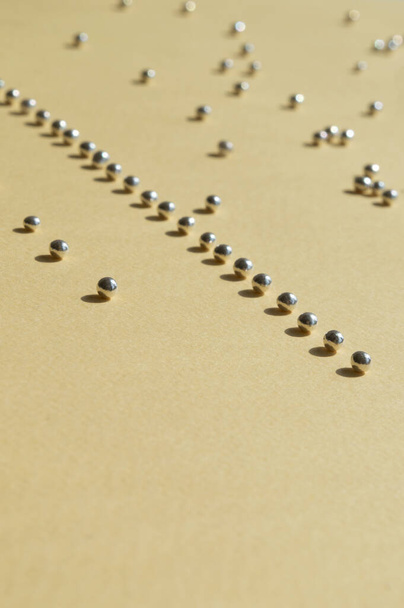 Rows of silver bakery beads with sunny shadows. Vertical photo with empty space down for necessary use. Geometry lines of sugar pearls on the light yellow background. Trendy concept idea. - Photo, Image